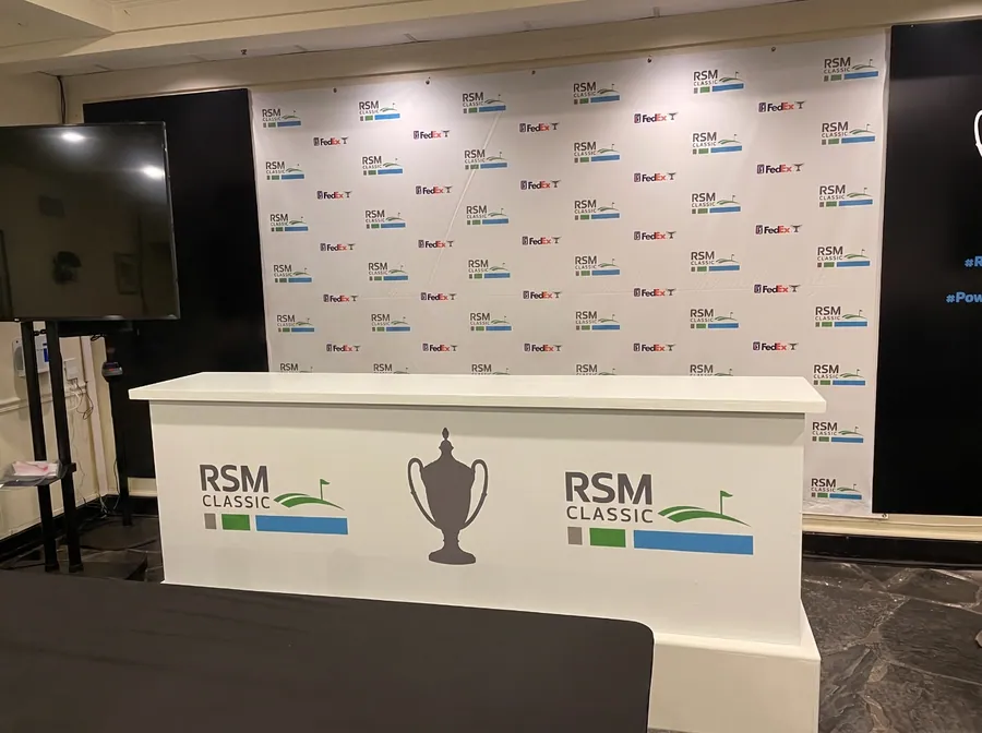 A press conference set with a repeat-pattern printed backdrop wall behind a fabricated podium counter carrying a tournament mark.