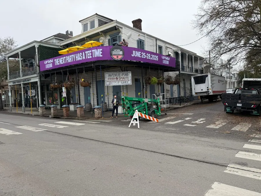 A crew installing a large printed banner across the front of a historic storefront, with a truck parked at the kerb.